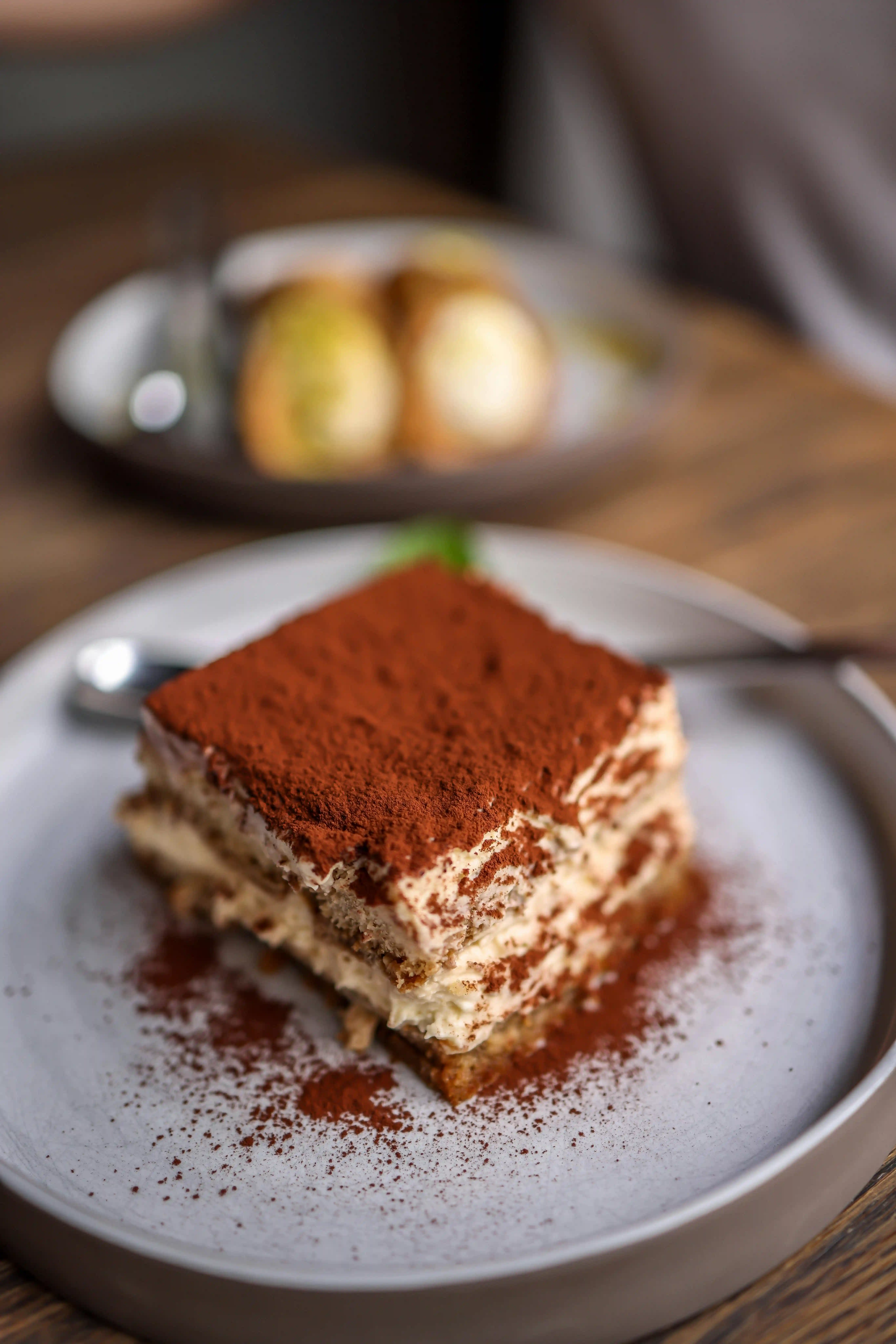 A decadent, layered slice of tiramisu sits on a grey plate and is heavily dusted with fine cocoa powder. This beautifully plated dish highlights the delicious results of a classic recipe for tiramisu dessert.